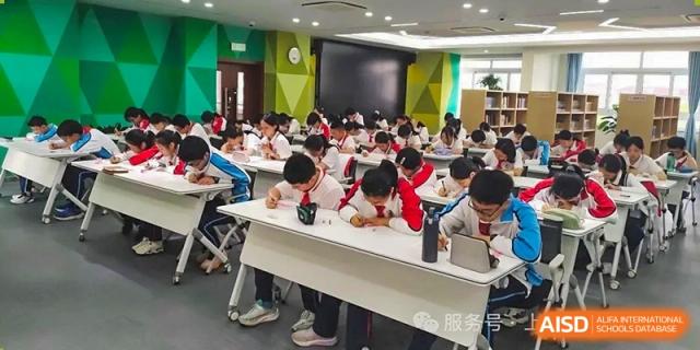 A wide shot of students seated at individual desks, working or studying quietly in a large classroom at Shanghai Nanyang Model Private School.