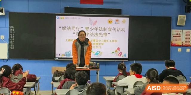A teacher standing next to a screen displaying text about youth legal education, lecturing students in a classroom at Shanghai Nanyang Model Private School.