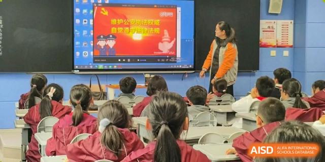 A teacher pointing towards a presentation on a large digital screen while addressing students seated in the classroom at Shanghai Nanyang Model Private School.