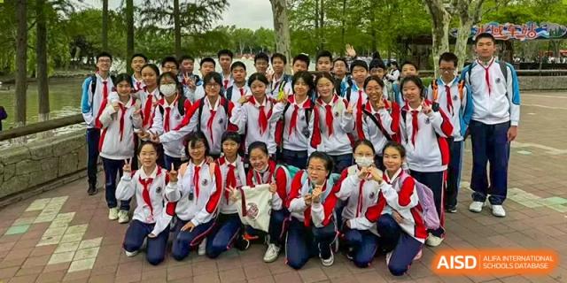 A large group of students in red and white uniforms posing happily for a group photo outdoors, likely on a field trip, at Shanghai Nanyang Model Private School.