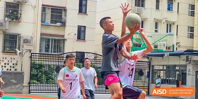 A student reaching up to catch or shoot a basketball outdoors during a game at Shanghai Nanyang Model Private School.