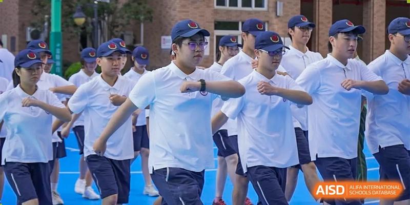 Students in white shirts and dark blue baseball caps running or marching in formation during a sports event at Shanghai Nanyang Model Private School.