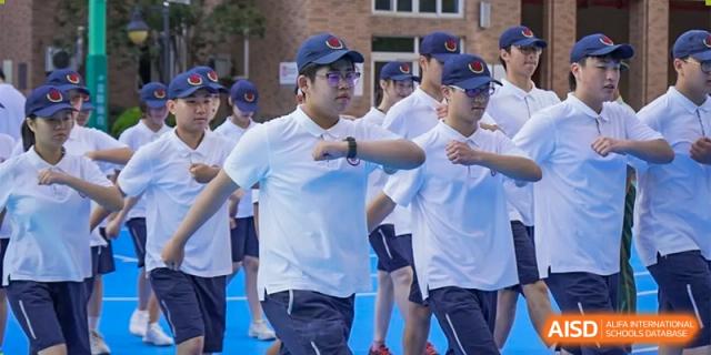 Students in white shirts and dark blue baseball caps running or marching in formation during a sports event at Shanghai Nanyang Model Private School.