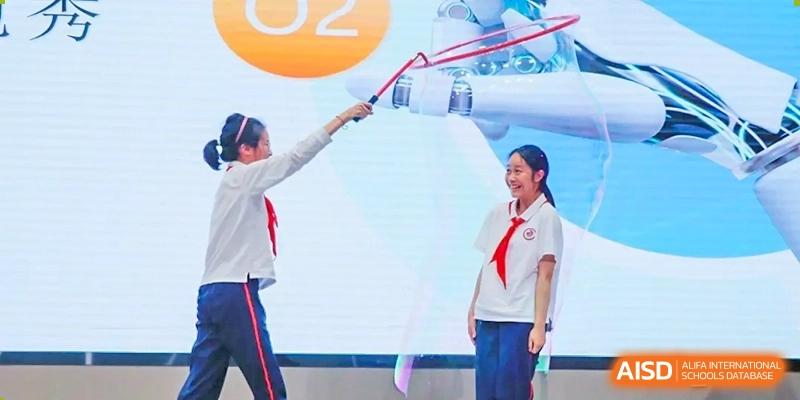 A student and a teacher holding a long red ribbon during a ceremony or event on a stage at Shanghai Nanyang Model Private School.