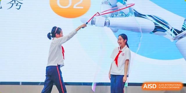 A student and a teacher holding a long red ribbon during a ceremony or event on a stage at Shanghai Nanyang Model Private School.