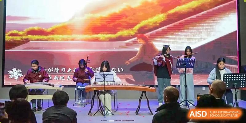 Students performing traditional music on stage, including a flute and a guzheng (Chinese zither), at Shanghai Nanyang Model Private School.