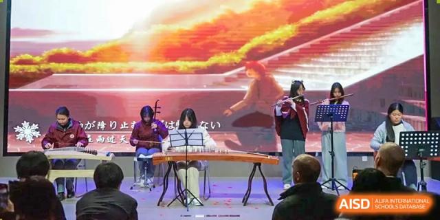 Students performing traditional music on stage, including a flute and a guzheng (Chinese zither), at Shanghai Nanyang Model Private School.