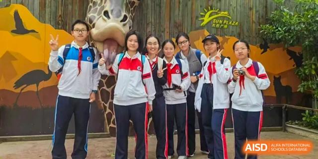 A small group of female students and teachers posing together outdoors with a large cartoon mascot visible at Shanghai Nanyang Model Private School.