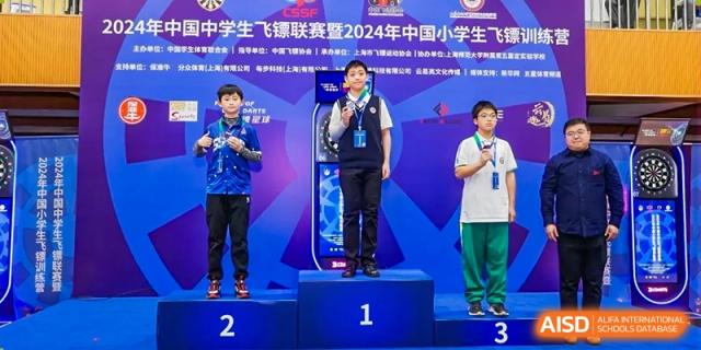 Students standing on a podium (1st, 2nd, and 3rd place) receiving awards at a competition or ceremony at Shanghai Nanyang Model Private School.