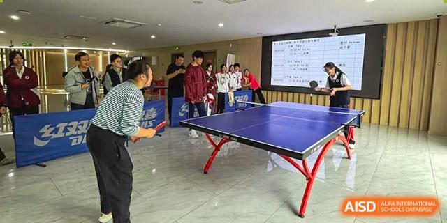 Students playing table tennis in an indoor activity area with a teacher supervising at Shanghai Nanyang Model Private School.