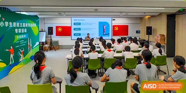 A view from the back of a Shanghai Pinghe School classroom where students in uniform are seated, listening to a presentation with the Chinese flag displayed.
