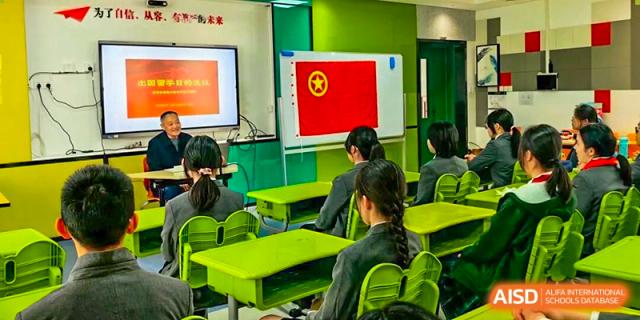 A classroom of Shanghai Pinghe School students in uniform attentively faces the front, where a screen displays the Chinese flag and a presentation.