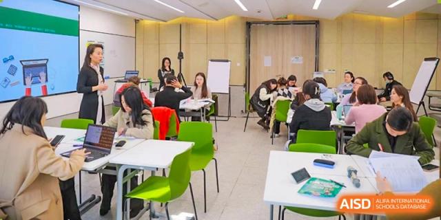 A teacher leads a discussion or workshop for a small group of Shanghai Pinghe School students seated at tables in a bright, modern room.