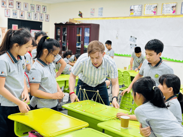 An international teacher helps a group of Shanghai Pinghe School students in uniform with an engaging, hands-on activity in a classroom.
