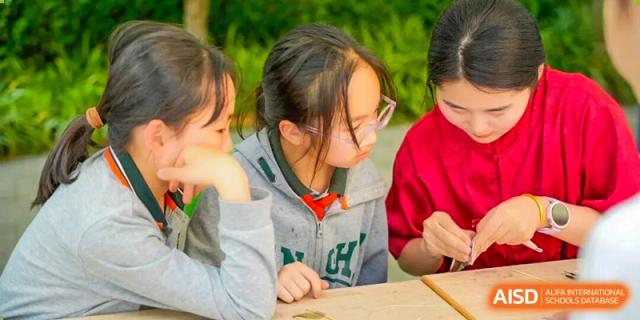A close-up of a group of Shanghai Pinghe School students, one wearing glasses, focused intently on a small object or activity on the table.