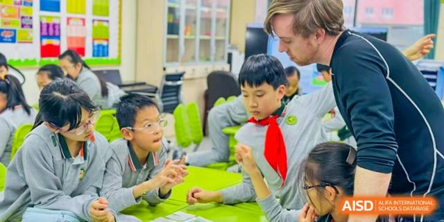 A group of Shanghai Pinghe School primary students in red scarves and uniforms collaborate with an international teacher on a project.