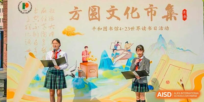 Two students in school uniform holding files and standing in front of a colorful banner or backdrop with Chinese text and illustrations at Shanghai Pinghe School.