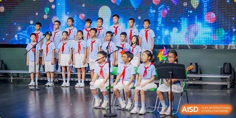 A large group of primary students in red scarves and uniforms lined up on a stage for a performance at Shanghai Pinghe School.