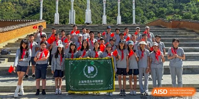 A large group of students in red scarves posing outdoors behind a banner with the school logo and Chinese characters for Shanghai Pinghe School.