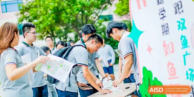 Students gathered outdoors, leaning over a table to sign or write on a document during a campus event at Shanghai Pinghe School.