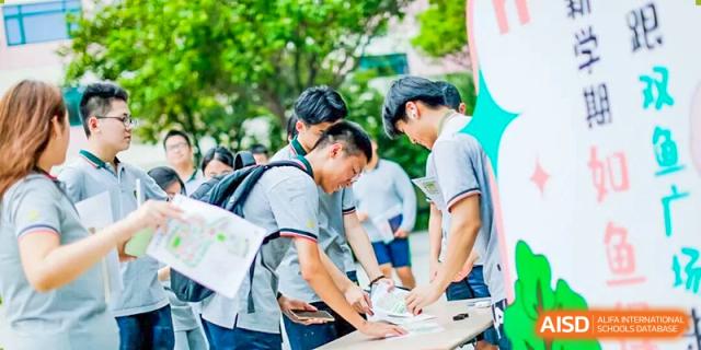 Students gathered outdoors, leaning over a table to sign or write on a document during a campus event at Shanghai Pinghe School.