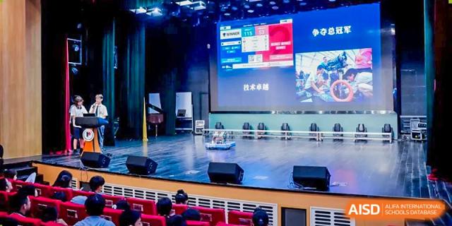An interior view of a stage in a dark, modern school auditorium with tiered seating at Shanghai Pinghe School.