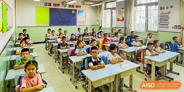 A wide shot of a classroom full of attentive young students sitting quietly at their desks facing the front at Beijing Bayi School International Department.