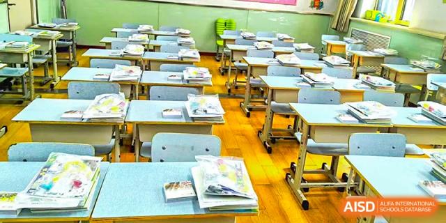 An empty classroom at Beijing Bayi School International Department showing rows of light-colored desks and chairs with books and materials neatly placed on the surfaces.