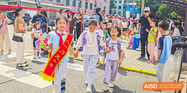Group of young students, including one wearing a red sash with Chinese characters, walking together outdoors near the Beijing Bayi School International Department.