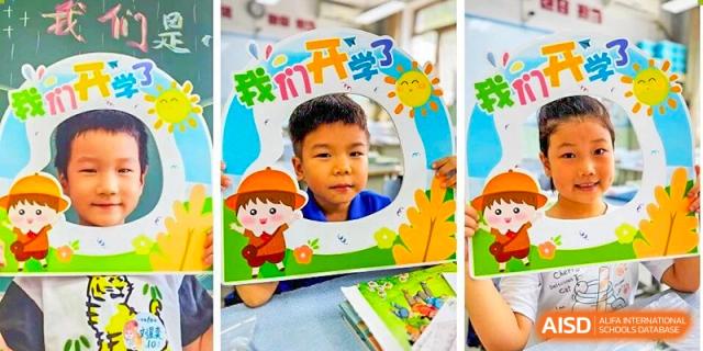 Beijing Bayi School International Department student looking through a celebratory cutout sign that says "开学" (Kāixué - Start of School) for the first day of school.