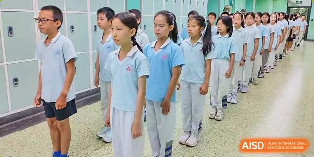 A line of female students in light blue and white uniforms standing formally outdoors, possibly during an assembly or sports event at Beijing Bayi School International Department.