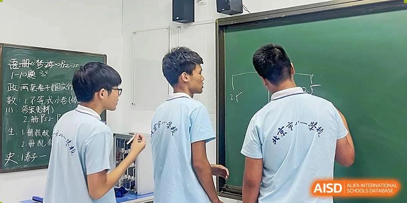Two male students from the Beijing Bayi School International Department facing a chalkboard or screen, engaged in a classroom activity or science demonstration.