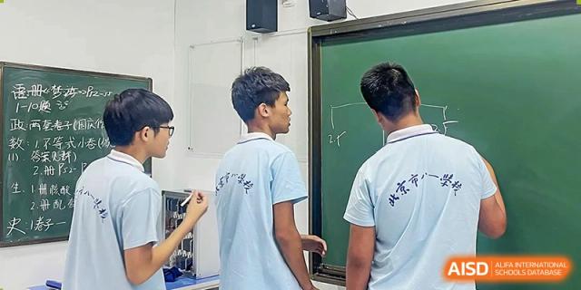 Two male students from the Beijing Bayi School International Department facing a chalkboard or screen, engaged in a classroom activity or science demonstration.