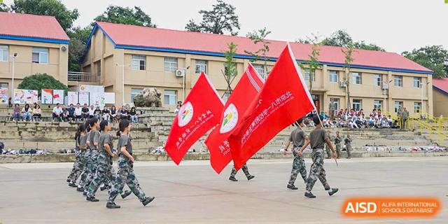 Students or military personnel marching past with large red flags during an outdoor ceremony or parade at the Beijing Bayi School International Department.