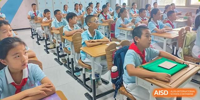 A close-up of students in light blue shirts sitting at wooden desks in a classroom, listening to a lesson at the Beijing Bayi School International Department.