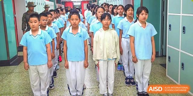 A close-up line of students, mostly in light blue shirts and white pants, standing outdoors in formation at the Beijing Bayi School International Department.