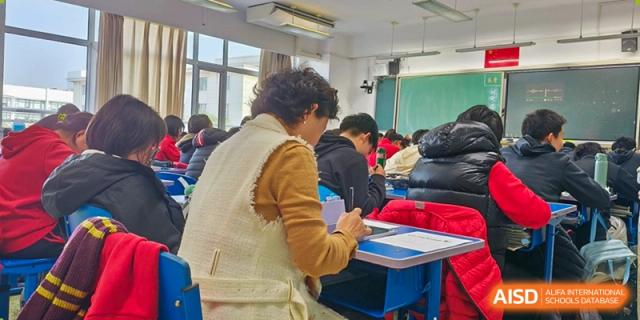 A teacher at Chengdu Experimental Foreign Languages School International Department walking among students and checking their work in a classroom.