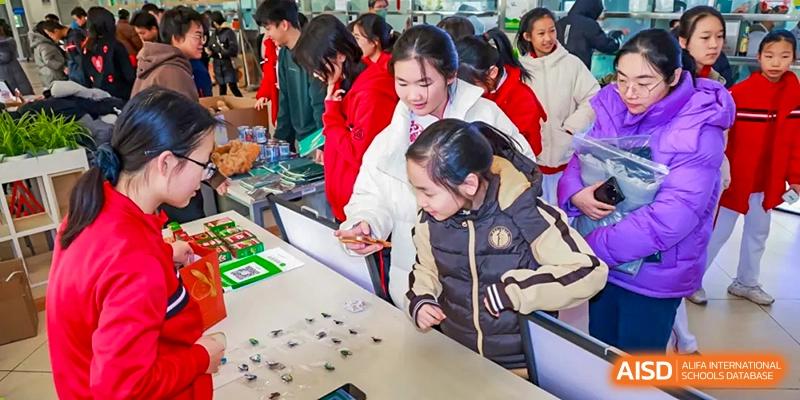 Chengdu Experimental Foreign Languages School International Department students engaging in an indoor activity, possibly a fair or market, with one student showing something on a table to others.