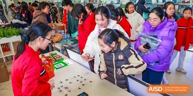 Chengdu Experimental Foreign Languages School International Department students engaging in an indoor activity, possibly a fair or market, with one student showing something on a table to others.