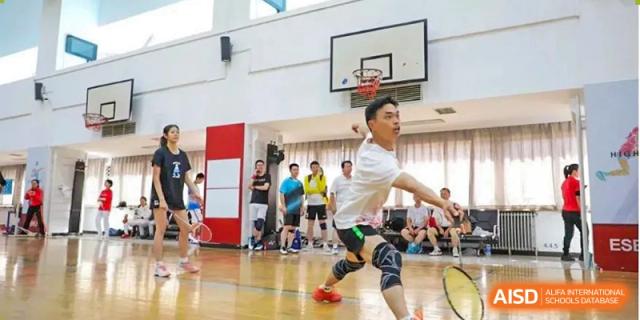 Chengdu Experimental Foreign Languages School International Department student playing badminton in an indoor gymnasium, with other students watching in the background.