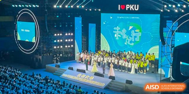 A large, lively performance or assembly at Chengdu Experimental Foreign Languages School International Department taking place on a large stage with "I ❤️ PKU" visible on the screen.