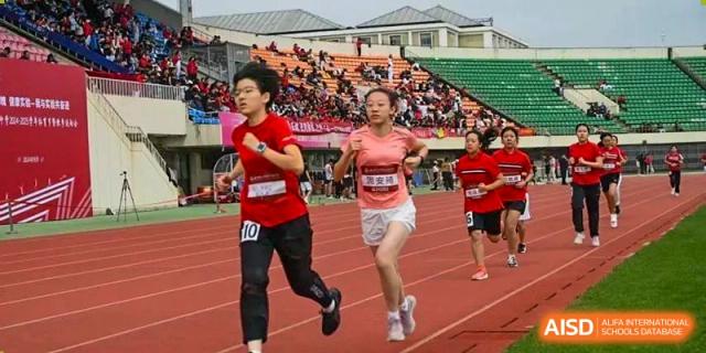 Chengdu Experimental Foreign Languages School International Department students running a race on the track during a sports meet, wearing red athletic gear.