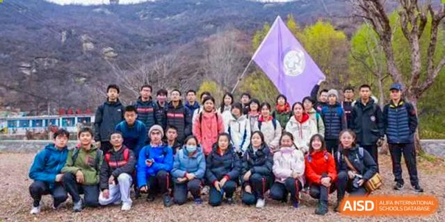 A large group of Chengdu Experimental Foreign Languages School International Department students and staff posing for a photo outdoors on a hill, holding a purple school flag.