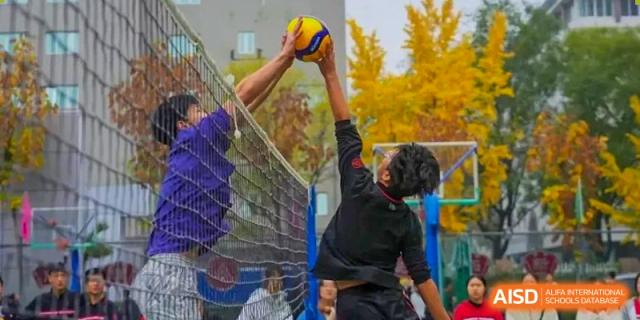 Two Chengdu Experimental Foreign Languages School International Department students playing volleyball outdoors, with one spiking the ball over the net.