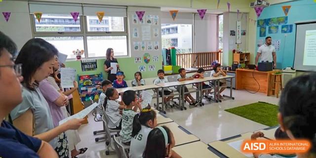 A busy, vibrant classroom scene with many students seated at tables doing activities at Shanghai Hongqiao International School.