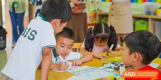 A teacher helping a young boy and girl with their schoolwork at a table at Shanghai Hongqiao International School.