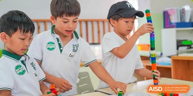 Two young boys, one wearing a baseball cap, smiling while interacting during a classroom activity at Shanghai Hongqiao International School.