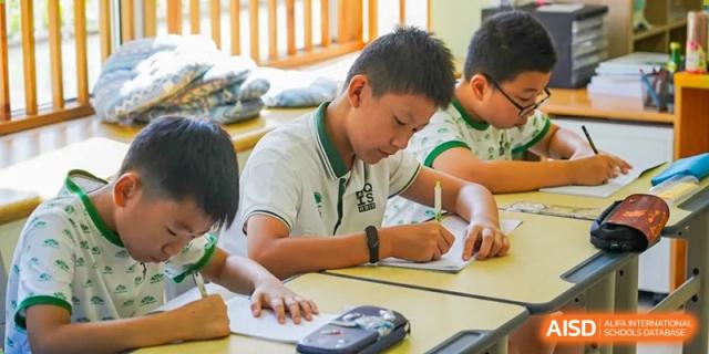 A student in a white polo shirt intently writing and taking notes at their desk at Shanghai Hongqiao International School.