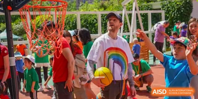 A teacher or student wearing a white t-shirt with a rainbow design, holding a basketball outdoors at Shanghai Hongqiao International School.