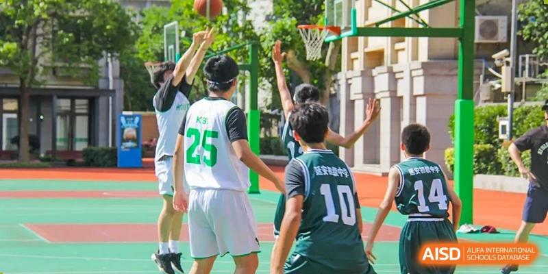 Students in sports uniforms actively playing basketball on an outdoor court at Shanghai Hongqiao International School.